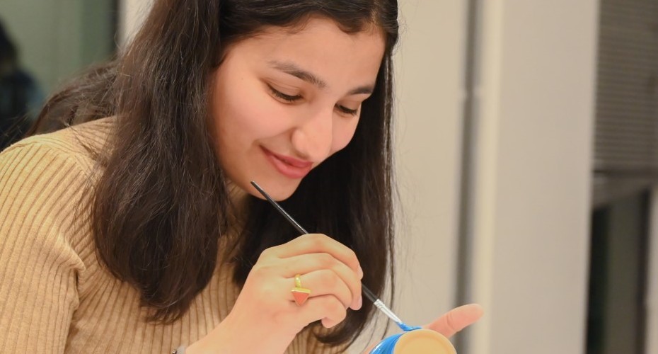 A person holds a toothbrush while painting a decorative cup with colorful designs.