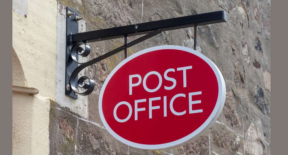 A metal bracket holding an oval shaped red and white sign which says Post Office