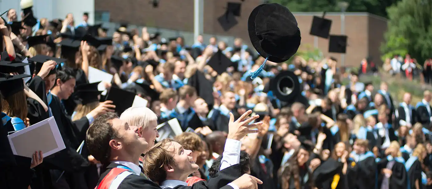 A large group of student throwing their motarboards in the air at the Streatham Campus piazza.