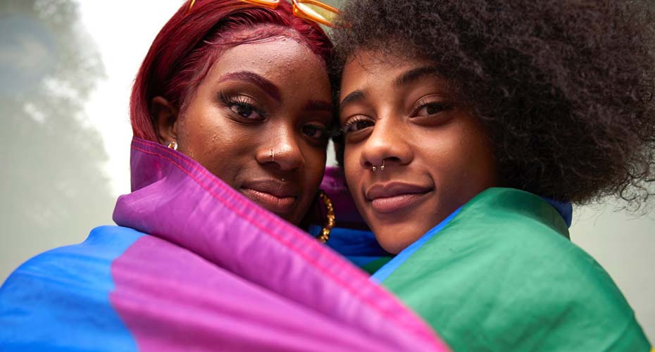 Young couple smiling at the camera draped in a lbgtq flag